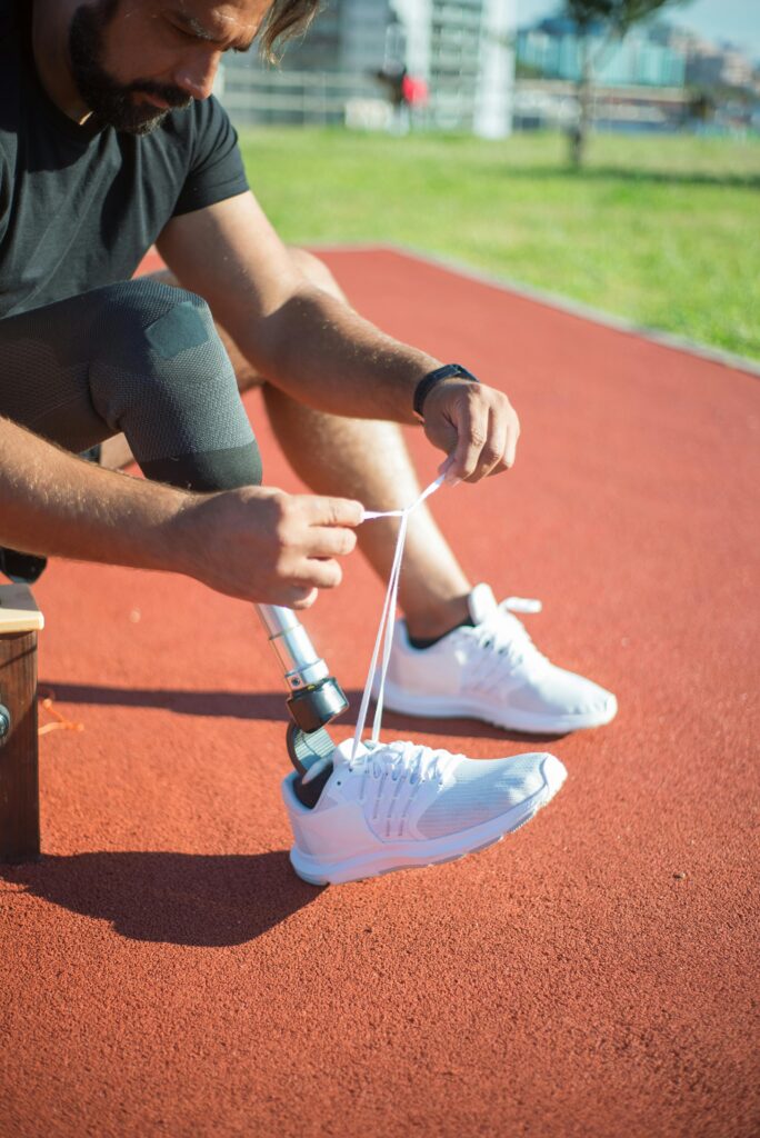 Male athlete with prosthetic leg ties a shoe on a sunny outdoor track, preparing for exercise.